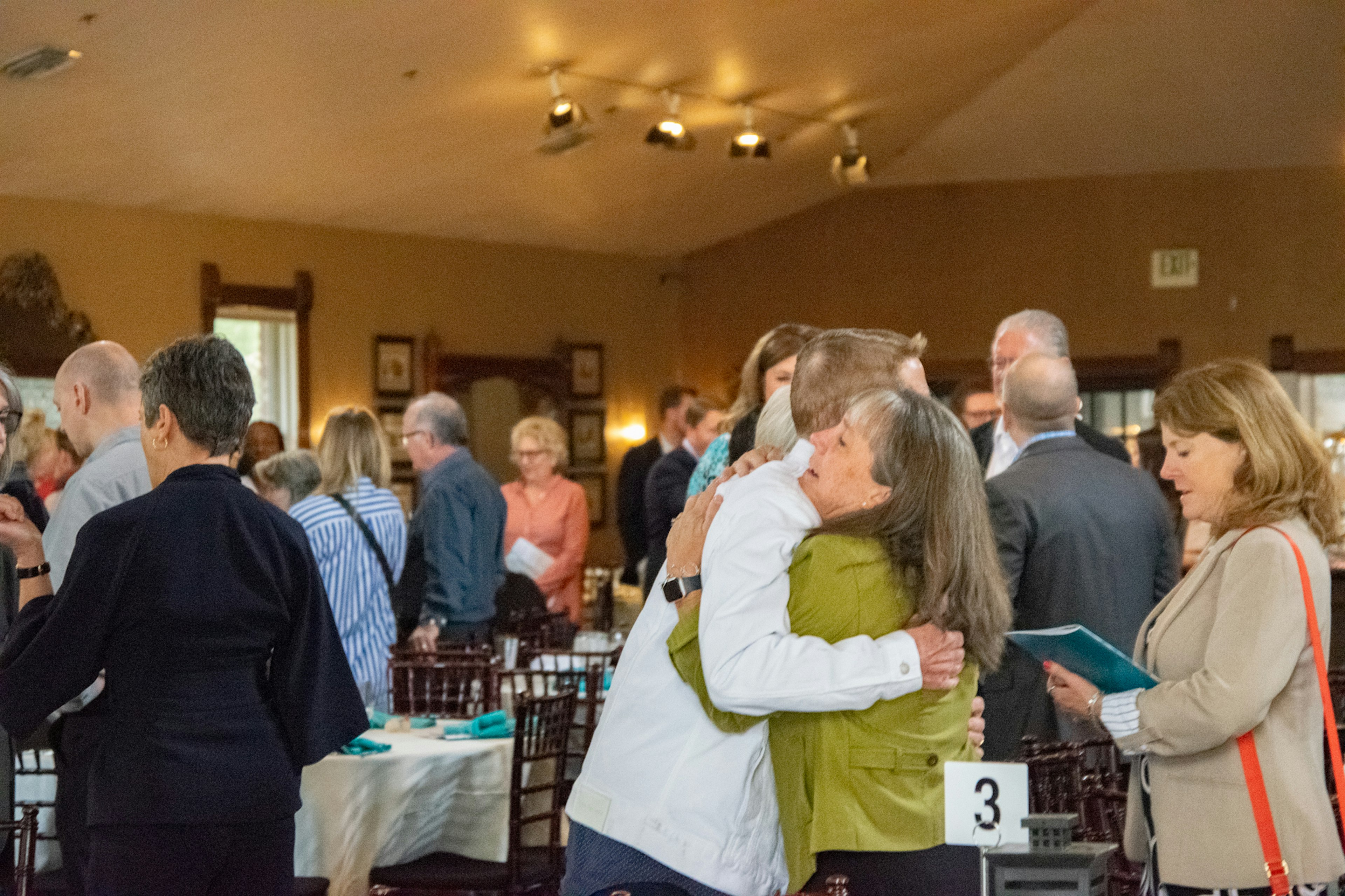 Community Breakfast: People congregating in dining room. Jen Leosz, Co-CEO, hugging attendee.
