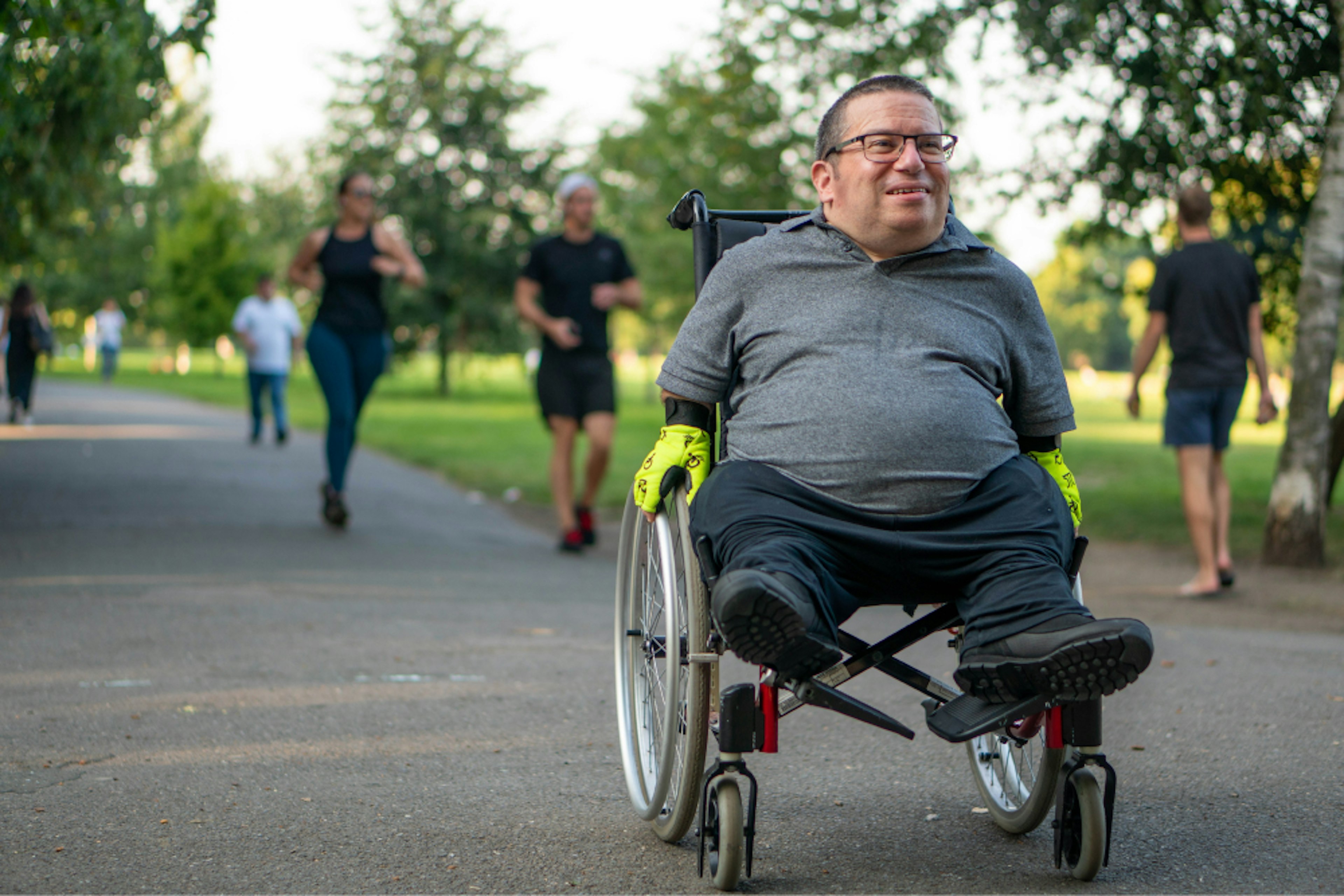 Pathway to Wellness Tile 1: Man in wheelchair on path in park.