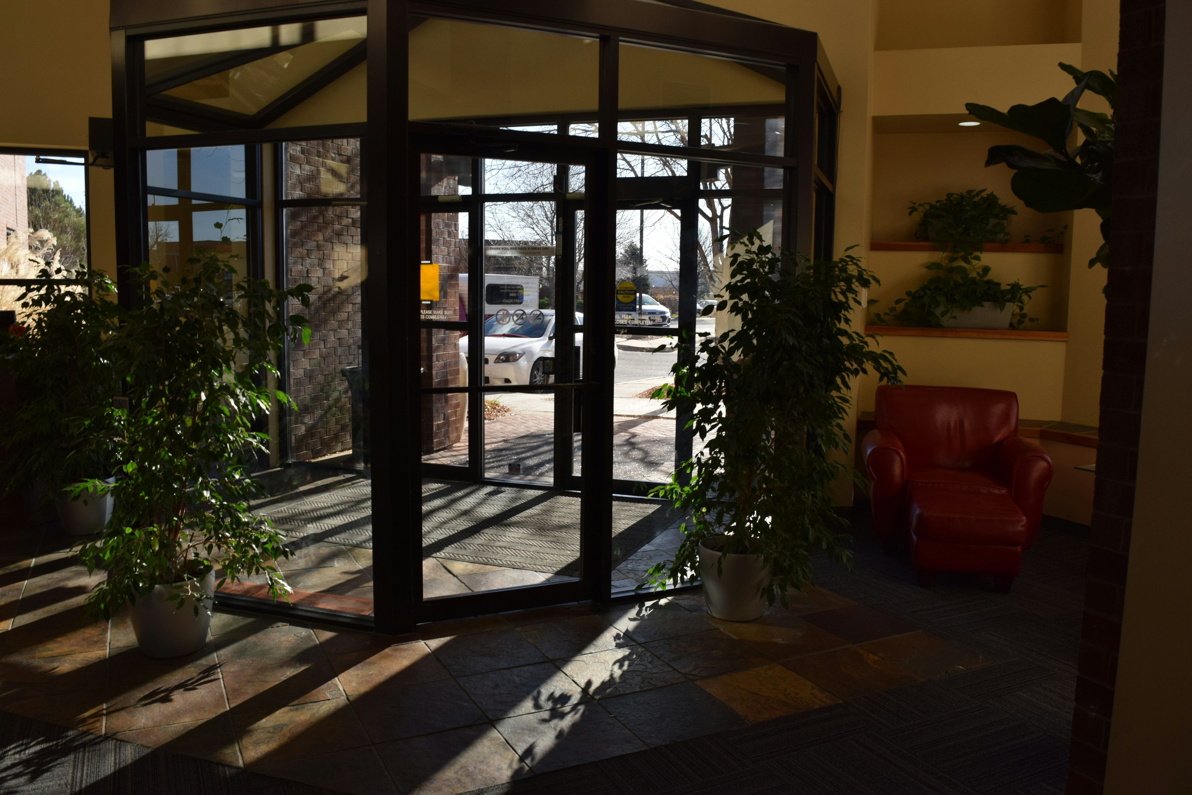 Inside of entry lobby to Dixon. Glass front doors, houseplants, yellow painted walls, and tile flooring.