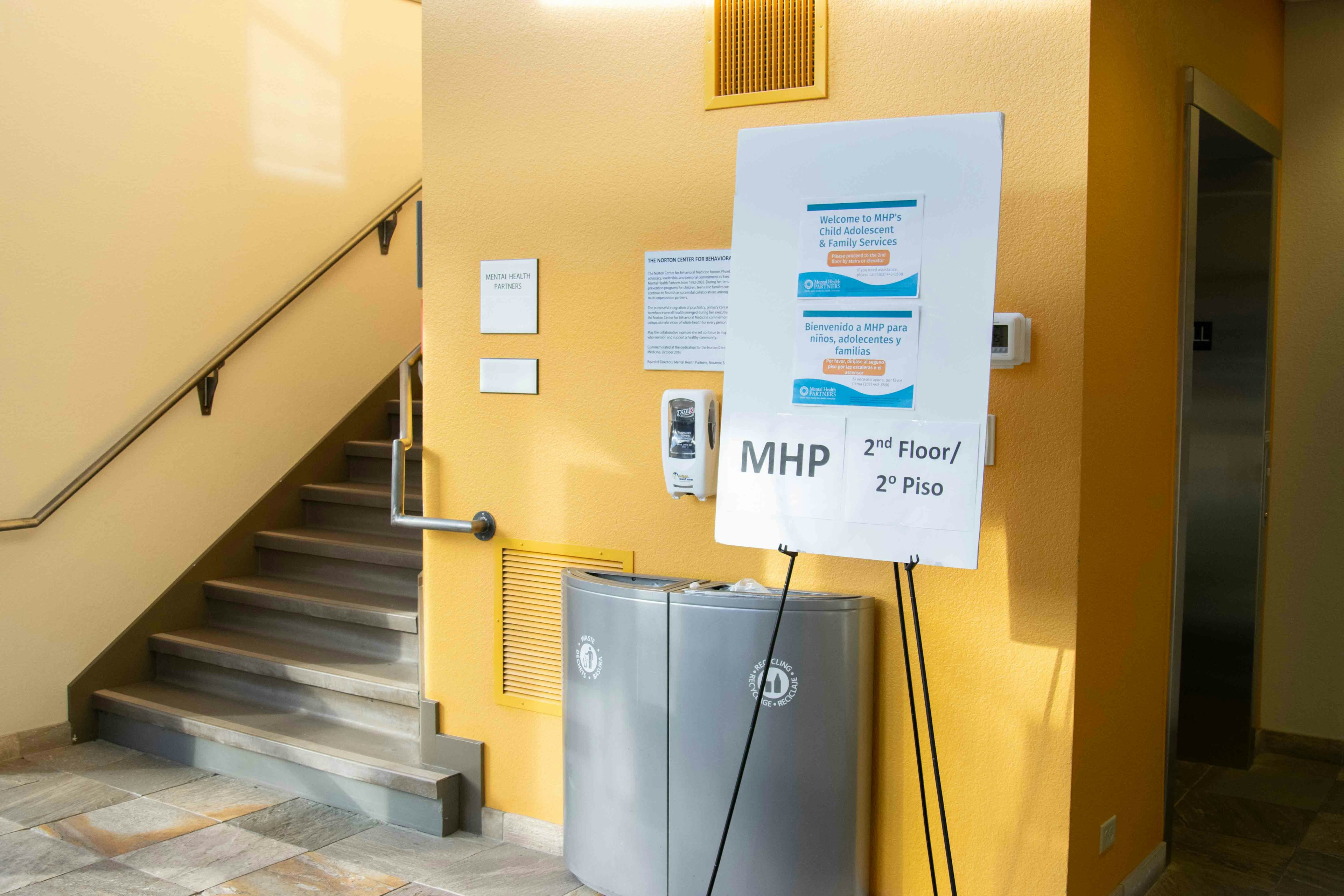 Entryway to Norton building. Bright yellow walls, sign that reads: MHP 2nd floor/2 Piso, and a staircase leading up to the second floor.