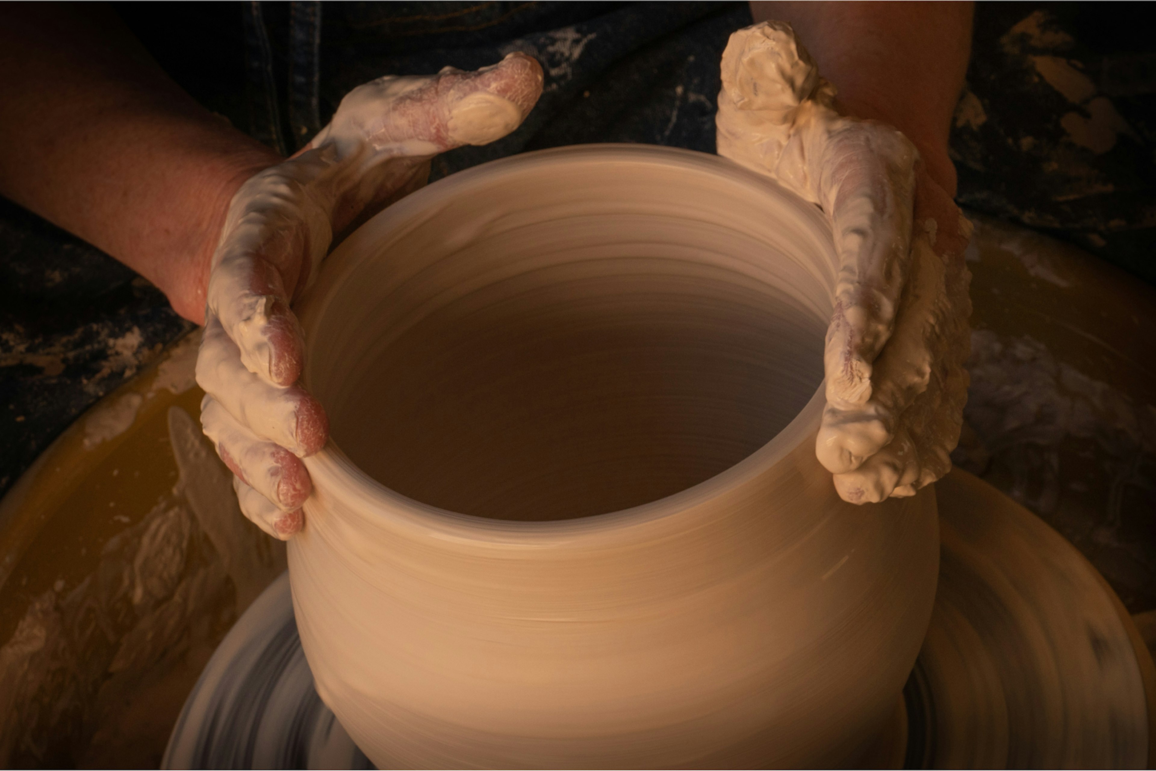Hands molding a clay pot.